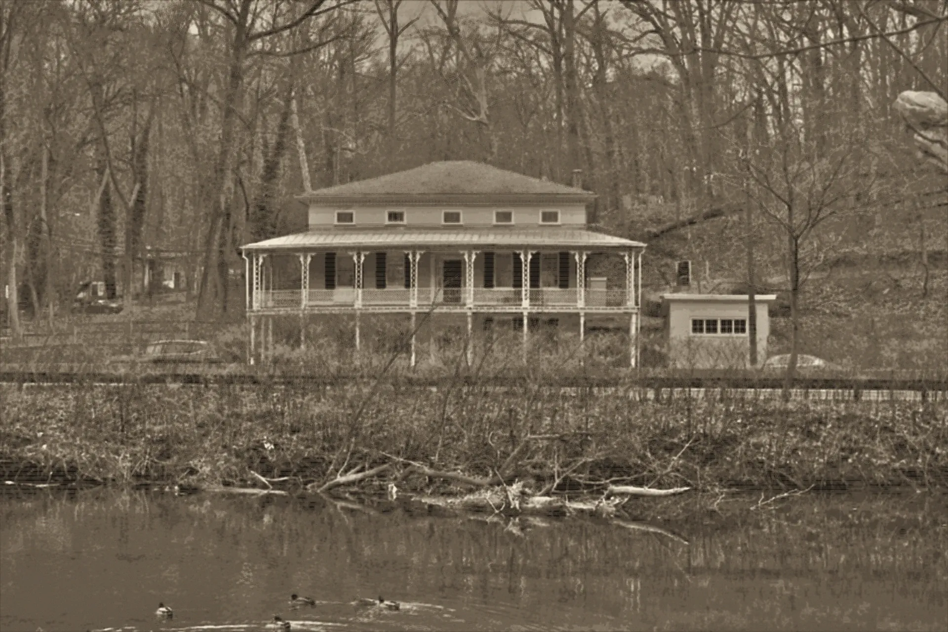 Wissahickon Hall at dusk, drawn from the keeper's own photograph of the house as it stands: a pale two-story hall raised on piers, its two-tier veranda lit, the creek in the foreground